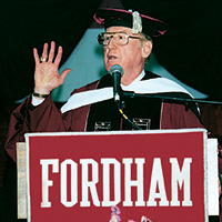 Fordham alumnus Vin Scully, wearing a graduation cap and maroon gown, delivers the commencement address to the Fordham University Class of 2000 in the Rose Hill Gym.