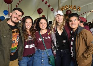 People standing under a decorated tent smiling in Fordham shirts