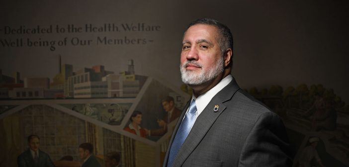 Fordham Law grad Mark Torres, general counsel for the Teamsters Union Local 810, stands in front of a New Deal-era, pro-union mural created by Auriel Bessemer. The text on the mural reads in part, "Dedicated to the Health, Welfare and Well-being of Our Members."