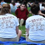 Two student volunteers sit on Edwards parade, leading orientaion. The backs of their shits say "Go forth and set the world afire"