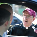 Joseph M. McShane, President of Fordham, greets a family through the driver side of a car arriving at the Rose Hill campus.