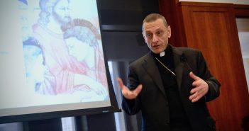 Bishop Caggiano gestures with his hands in front of a PowerPoint slide.