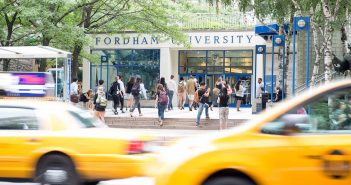 People walk in front of the entrance to Fordham's Lowenstein Center, as two yellow cabs pass in the foreground.