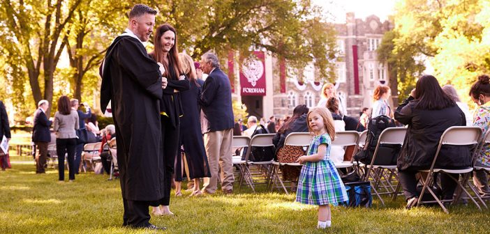 Little girl in blue dress facing man and woman in academic robes