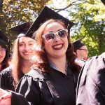 Line of graduates wearing black academic gowns, including a woman with white sunglasses