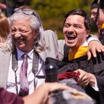 A male graduate laughs as older man in tie puts his arm around his shoulder