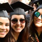 three women with black graduation caps, two in sunglasses