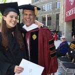 A graduate wearing a black academic robe poses fora picture with Tim Shriver, wearing a red academic gown