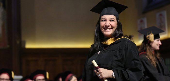 A woman holds a scroll while wearing a black academic robe.