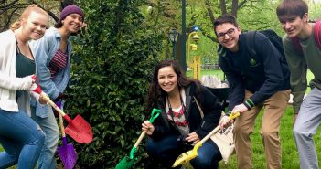 Five Fordham students pose in front of a newly planted holly tree with colorful shovels.