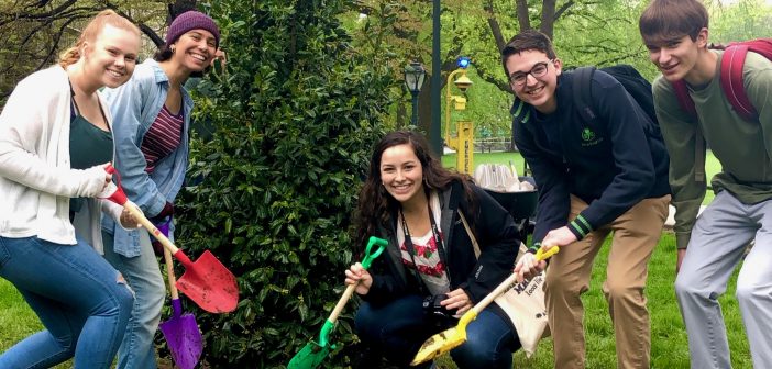 Five Fordham students pose in front of a newly planted holly tree with colorful shovels.