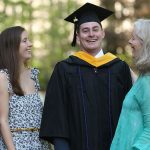 A graduate smiles for the camera as his family looks on