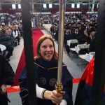 A woman wearing a faculty graduation gown holds a pole