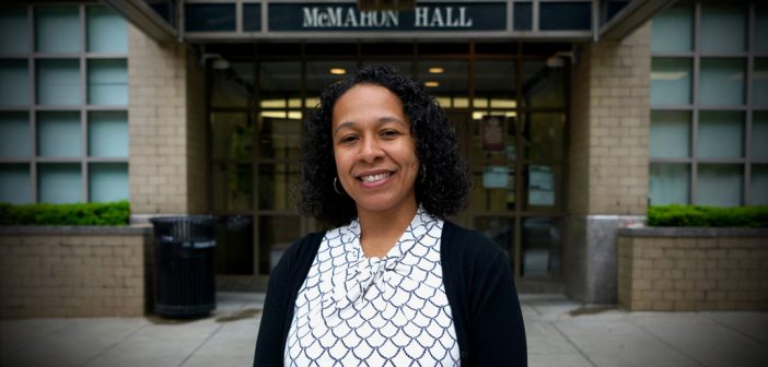A woman wearing a blouse and a dark cardigan smiles in front of McMahon Hall.