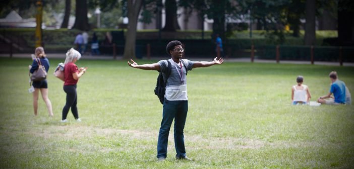 A student stands and thrusts out his arms on a field.