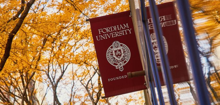 A Fordham flag in front of fall foliage