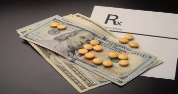 Pills are displayed on top of dollar bills to represent the costs of prescription drugs.