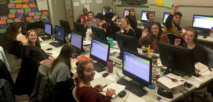 Students sitting in front of computers, wearing headsets and smiling at the camera