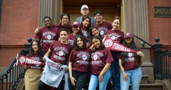 A group of teenagers wearing Fordham gear on the steps of Cristo Rey New York High School