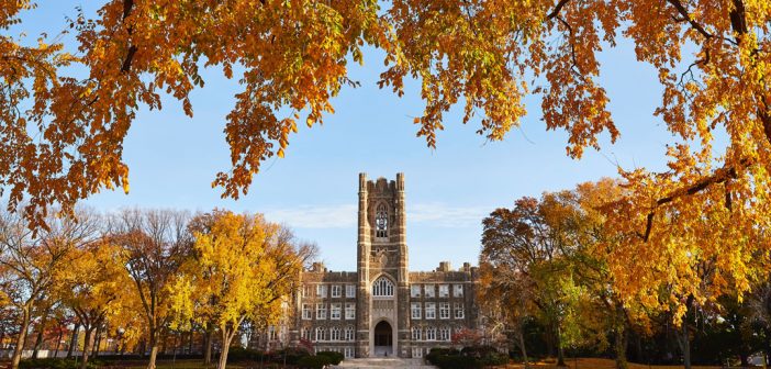 A big, Gothic-style building surrounded by orange autumn branches