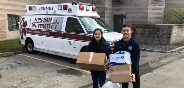 Two students hold boxes in front of an ambulance.