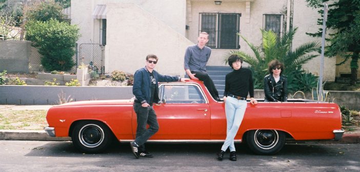 A promo photo of Car Seat Headrest posing on a red car.