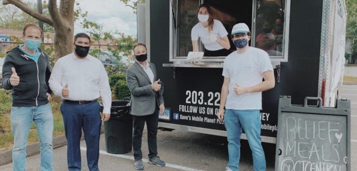 Five people standing by or in a food truck, wearing masks and giving a thumbs-up