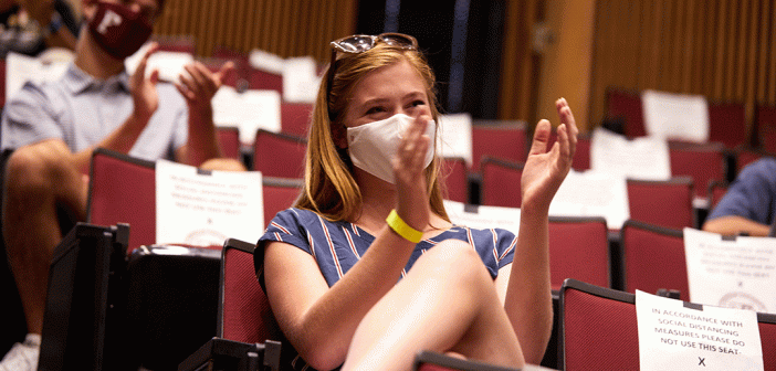 Masked woman clapping in auditorium surrounded by empty seats