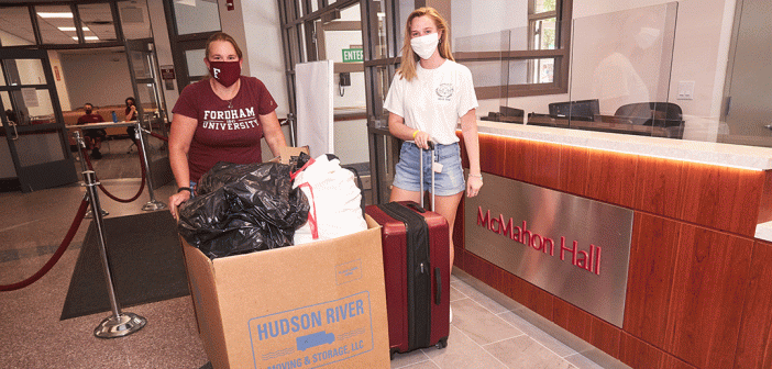 Two women in face masks stand with belongings in McMahon Hall