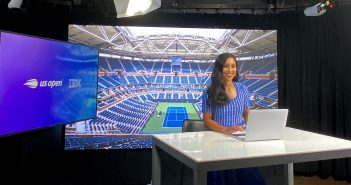 A woman wearing a blue dress smiles in front of a screen picturing an empty tennis court.