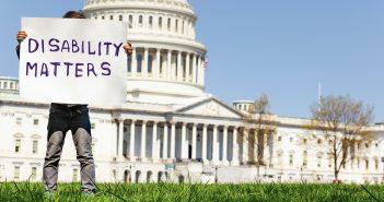 A boy stands in front of the Capitol Building and holds a handmade sign that says "DISABILITY MATTERS."