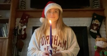 A young woman wearing a red Santa hat holds a taper candle and smiles at the camera.