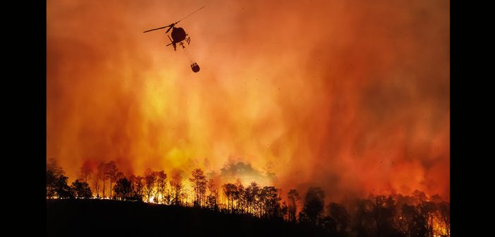 A helicopter flying above a burning landscape