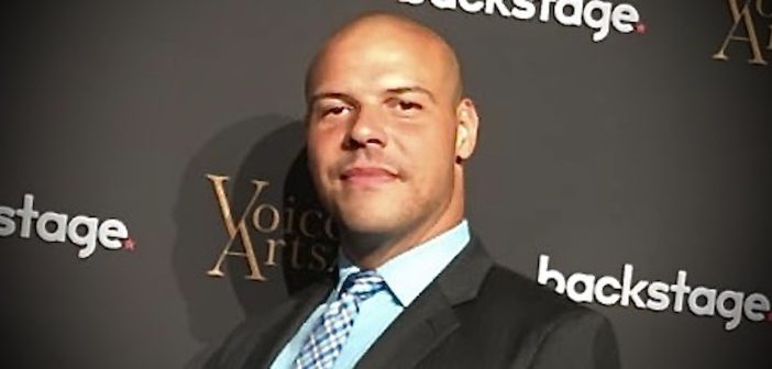 A man wearing a suit and tie smiles at the camera.