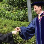A graduate fist bumping a faculty member.