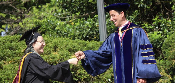 A graduate fist bumping a faculty member.