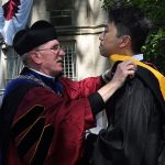 Father McShane adjusts the sash of a graduate