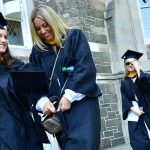 Two women wearing black graduation gowns smile while they walk.
