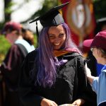 A female graduate with purple haair accepts her dimpoma