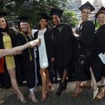 Eight women wearing black graduation gowns smile at the camera.
