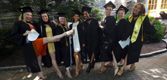 Eight women wearing black graduation gowns smile at the camera.