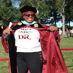 Woman graduate showing off a shirt under her gown that says "Dr."