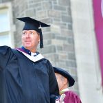 A male graduate waves from Keating Terrace