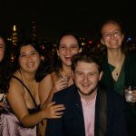 A group of recent Fordham graduates on the Young Alumni Yacht Cruise, October 2021, with the Manhattan skyline in the background