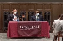 two men in masks at table giving lecture