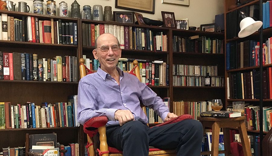 Father Raymond A. Schroth sits in a rocking chair in his room in Murray-Weigel Hall, surrounded by shelves of books, 2017