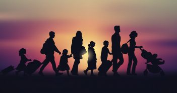 Silhouettes of a family of six walking in one direction in front of a sunset or sunrise