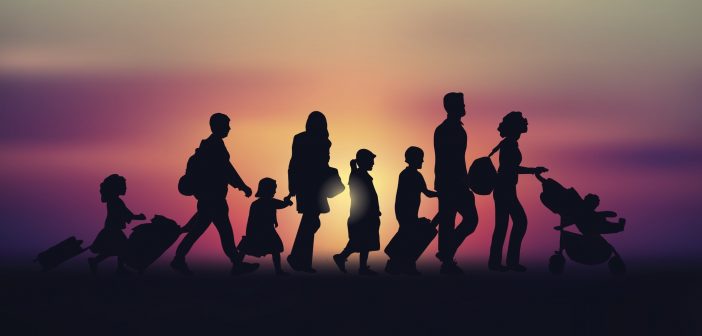 Silhouettes of a family of six walking in one direction in front of a sunset or sunrise