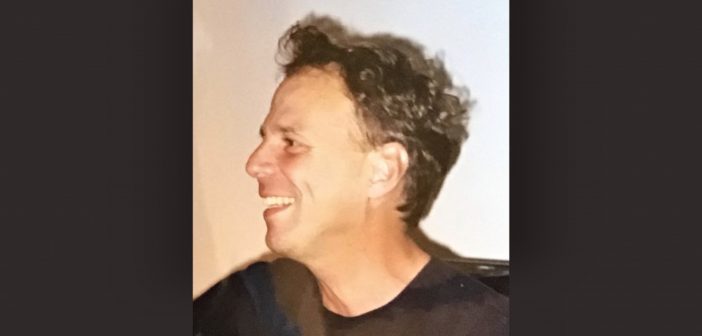 A side profile of a smiling man wearing a black shirt