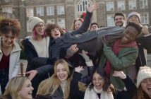 A group of students smile and laugh while holding up another student sideways.